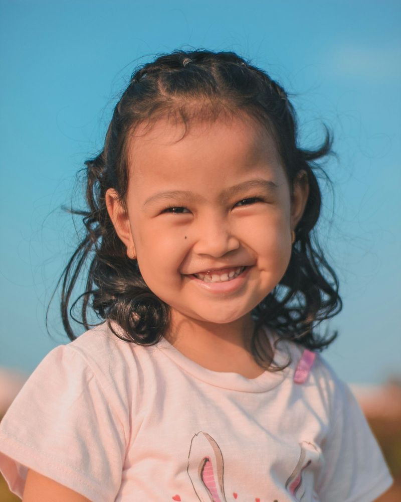 Anak perempuan berambut ikal tersenyum lebar