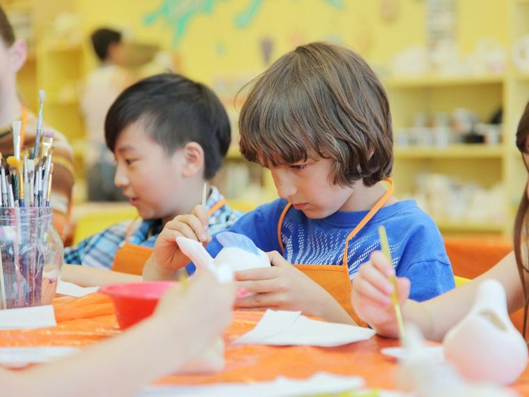 Anak-anak mewarnai patung keramik kecil di meja oranye