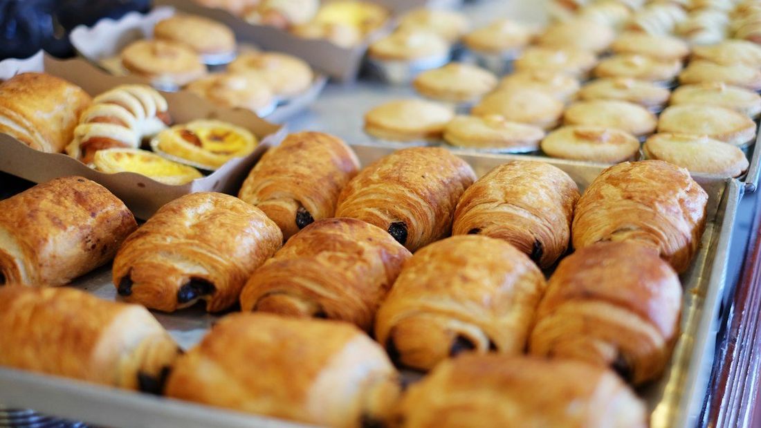 Nampan berisi croissant cokelat, roti bulat, dan pastry di etalase toko