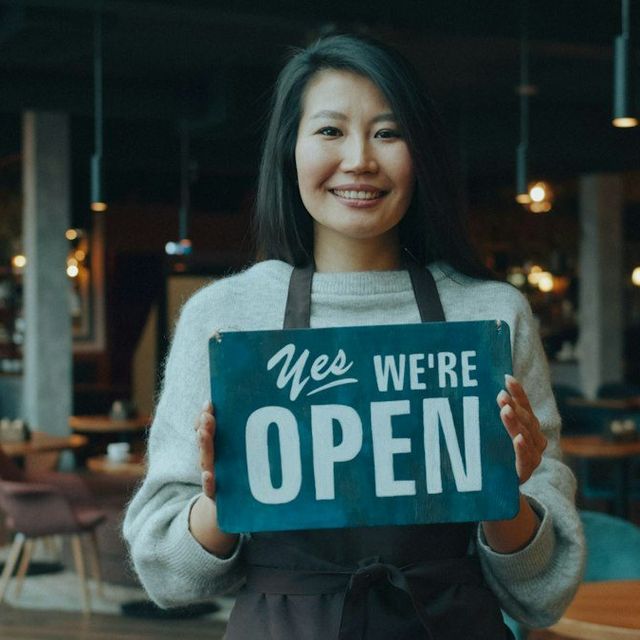 Pemilik kedai tersenyum memegang papan bertuliskan buka